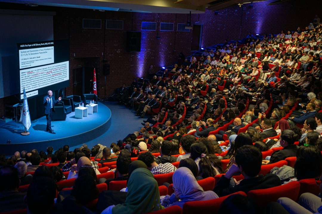 Man presents a scientific paper on a blue stage to an audience.
