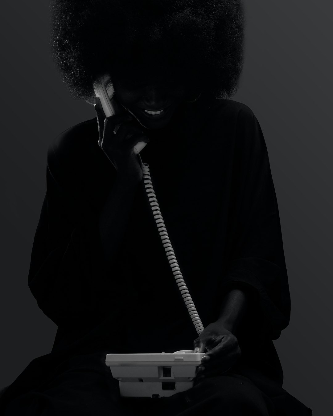 A person with an afro smiles while using a vintage telephone.