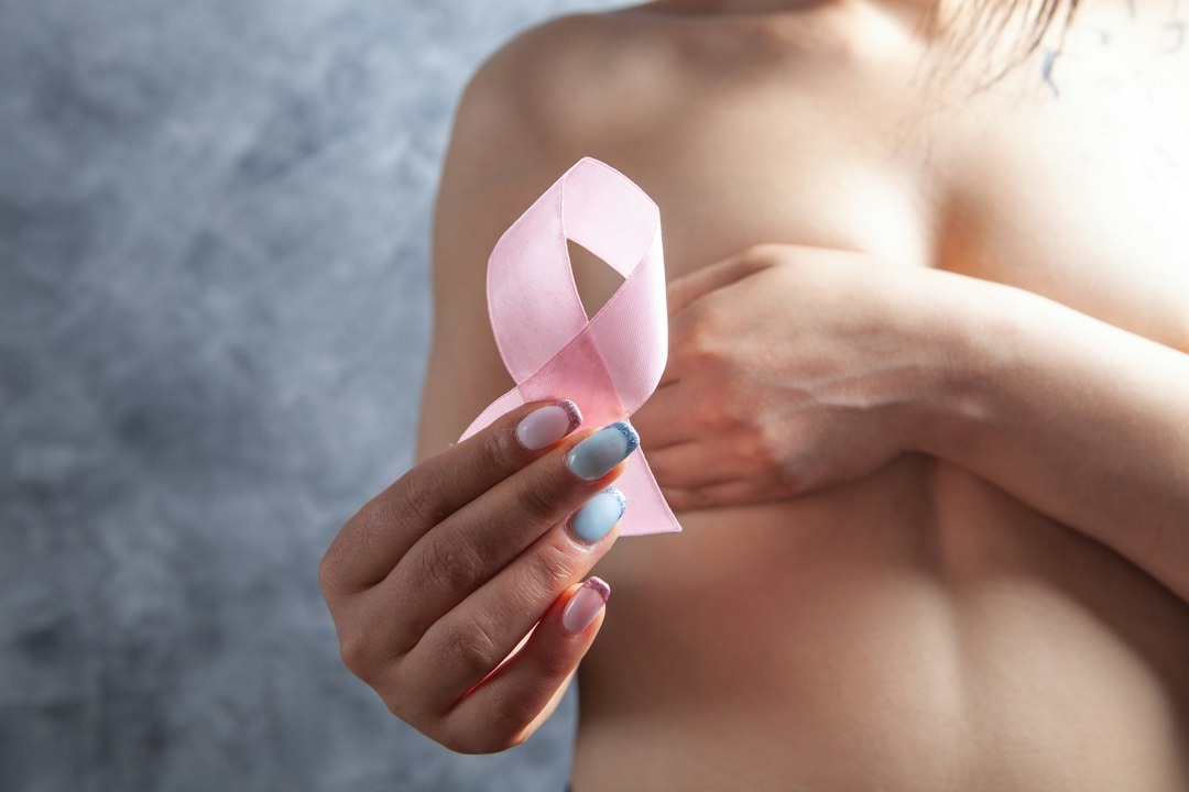 A hand holds a pink ribbon against their chest.