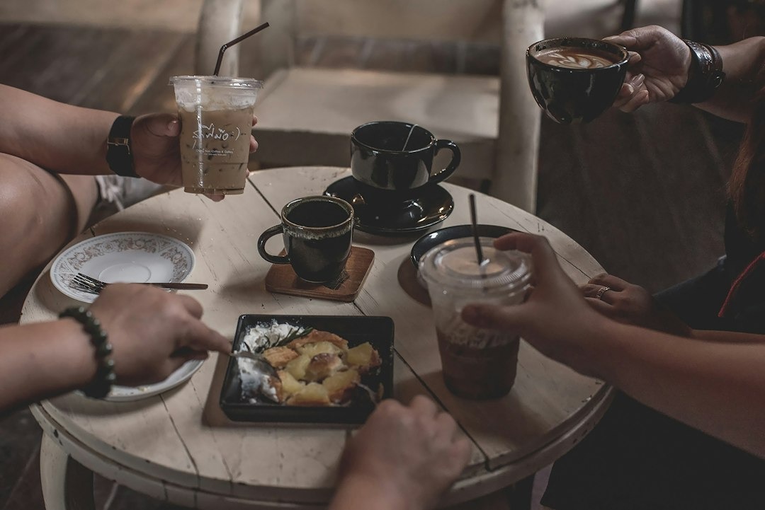 Friends share coffee and dessert around a wooden cafe table.